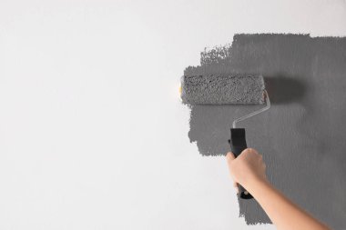 Woman painting white wall with grey dye, closeup. Space for text clipart