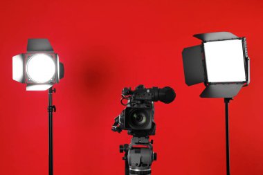 Kırmızı arkaplanda profesyonel video kamera ve ışıklandırma ekipmanları