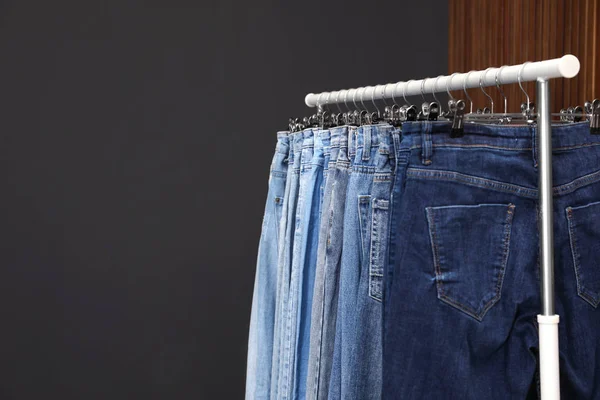 Rack with different jeans on dark grey background. Space for tex — 스톡 사진