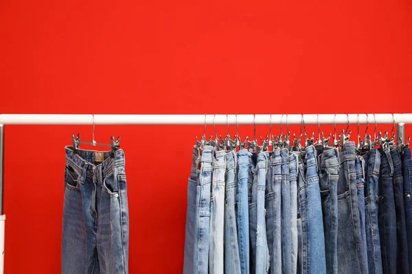 Rack with stylish jeans on red background — Stock Photo, Image