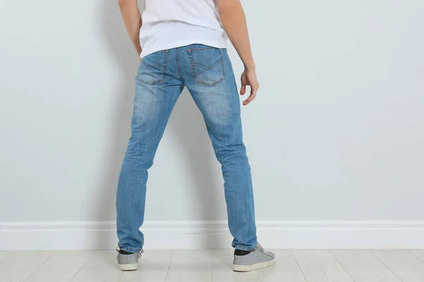 Młody mężczyzna w stylowych dżinsach przy lekkiej ścianie, zbliżenie — Zdjęcie stockowe