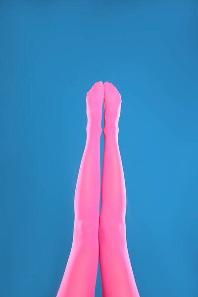 Woman wearing pink tights on blue background, closeup of legs