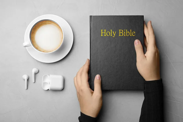 聖書を持つ女性 軽い灰色のテーブルでコーヒーやイヤホンのカップ トップビュー 宗教書 — ストック写真