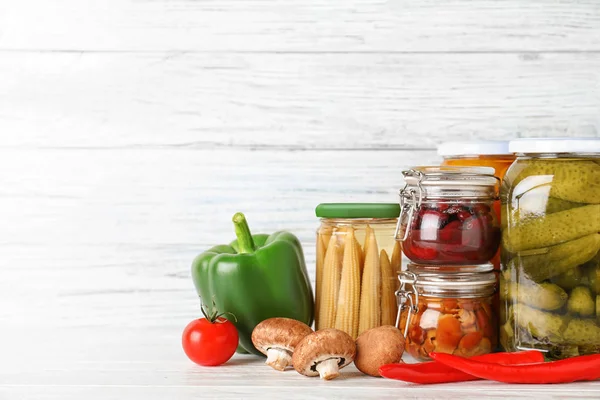 Frascos de vidrio con diferentes verduras en vinagre en lengüeta de madera blanca — Foto de Stock