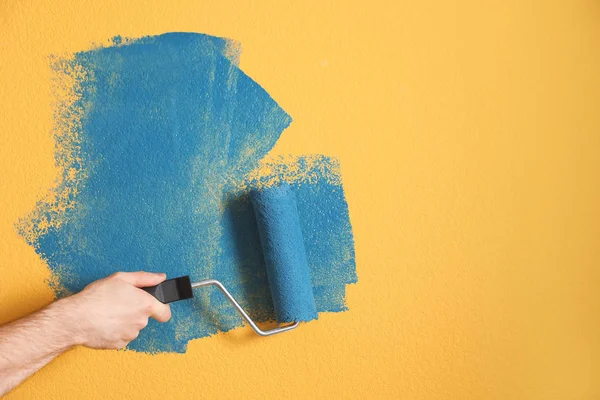 Muž malování žlutá stěna s modrým barvivem, detailní záběr — Stock fotografie