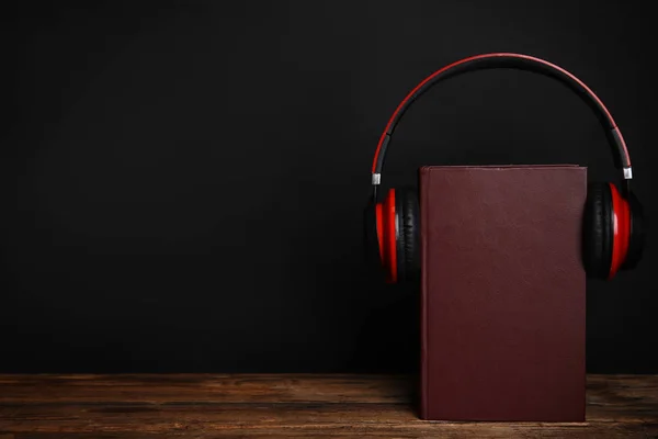 Libro y auriculares modernos en mesa de madera contra backgro negro —  Fotos de Stock