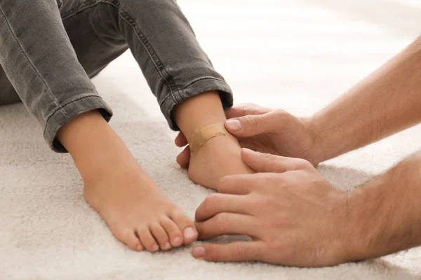 Father putting sticking plaster onto little son\'s leg indoors, closeup