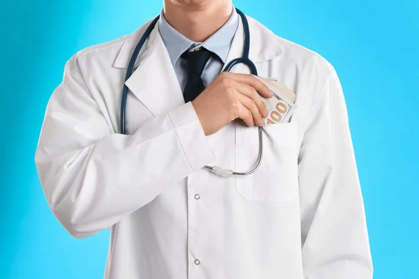 Médico poniendo soborno en el bolsillo sobre fondo azul claro, cerca —  Fotos de Stock