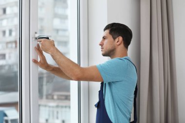 İnşaat işçisi plastik pencereyi elektrikli tornavidayla tamir ediyor.