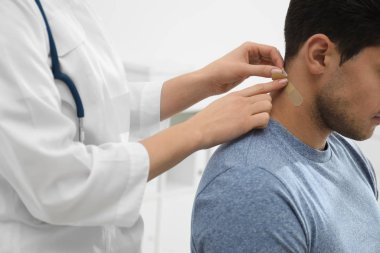 Doktor adamın boynuna sıva yapıştırıyor. Kapalı alanda, yakın plan.