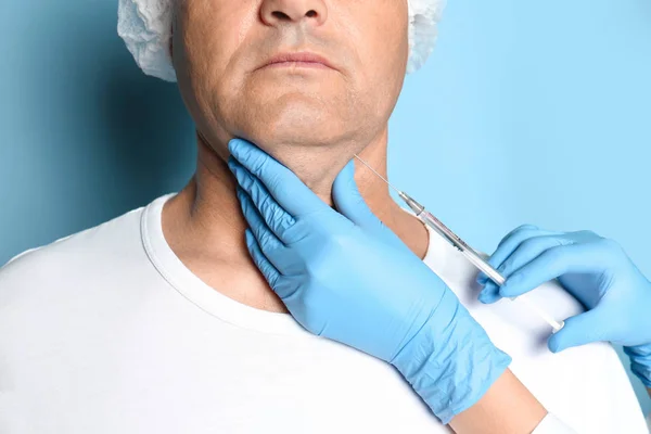 Mature man with double chin receiving injection on blue backgrou