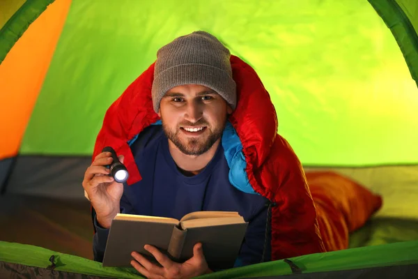 Ung man med ficklampa läsa bok i tält — Stockfoto