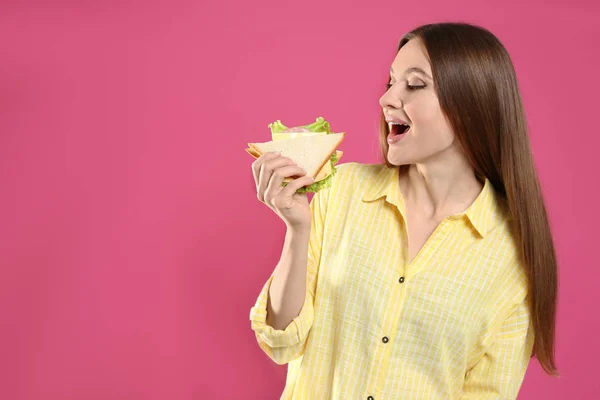 Mujer joven comiendo sabroso sándwich sobre fondo rosa —  Fotos de Stock