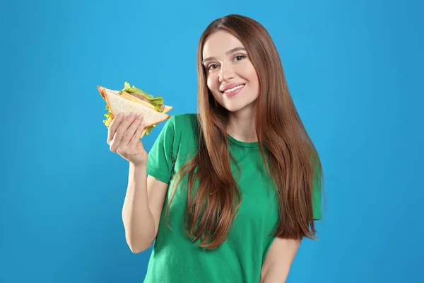 Młoda kobieta ze smaczną kanapką na jasnoniebieskim tle — Zdjęcie stockowe