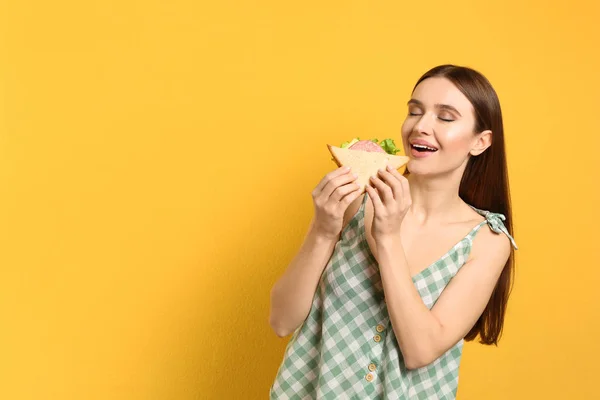 若い女性は黄色の背景においしいサンドイッチを食べる。スペースフォー — ストック写真