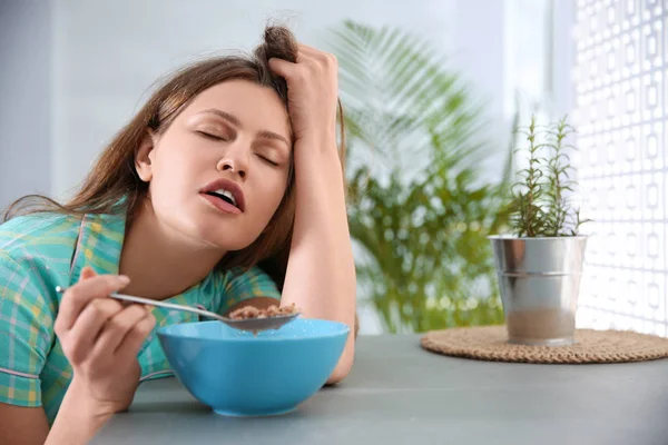 Sleepy young woman eating breakfast at home in morning — Stock Photo, Image