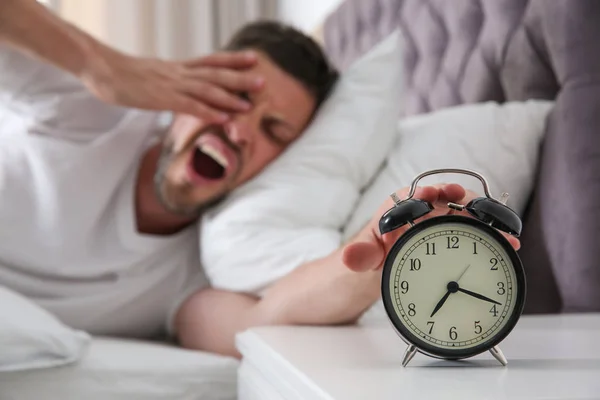 Sleepy man turning off alarm clock at home in morning, focus on — Stock Photo, Image
