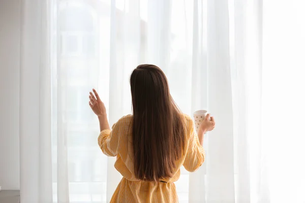 Giovane donna con coppa vicino alla finestra al chiuso — Foto Stock