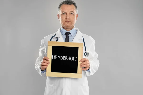 Doctor Sosteniendo Pizarra Con Palabra Hemorrhoid Sobre Fondo Gris Claro — Foto de Stock