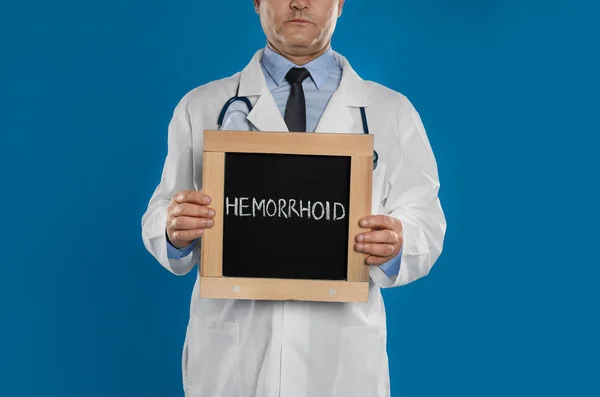 Doctor Sosteniendo Pizarra Con Palabra Hemorrhoid Sobre Fondo Azul Primer — Foto de Stock