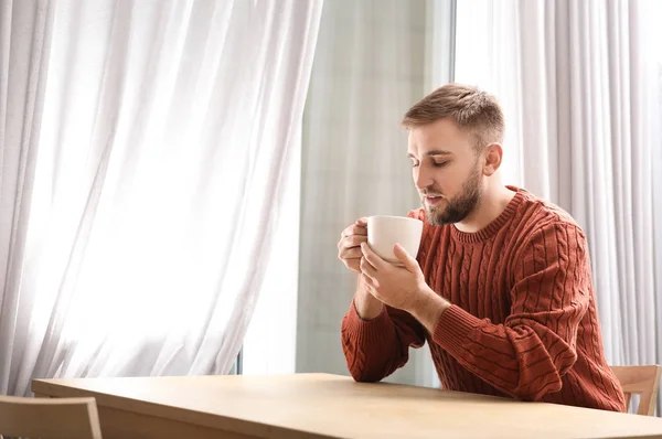 Young man with cup of hot drink near window at cafe — Stock Photo, Image