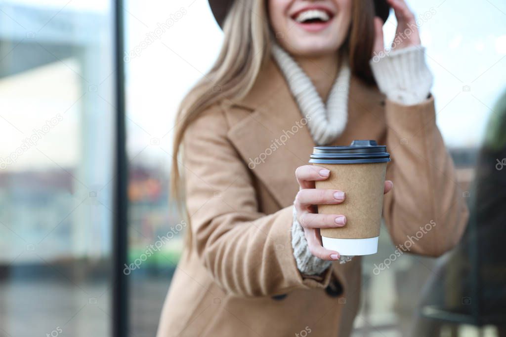 Young woman with cup of coffee on city street in morning, focus 