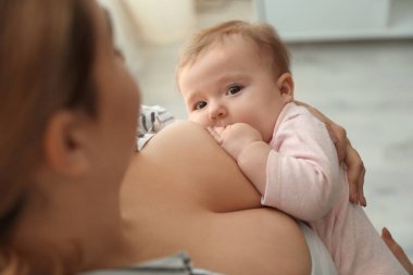 Genç bir kadın bebeğini evde emziriyor.