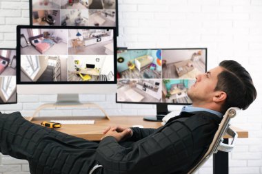 İş yerindeki monitörlerin yanında dinlenen erkek güvenlik görevlisi