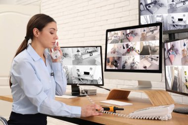 İş yerindeki monitörlerin yanında telefonla konuşan kadın güvenlik görevlisi.