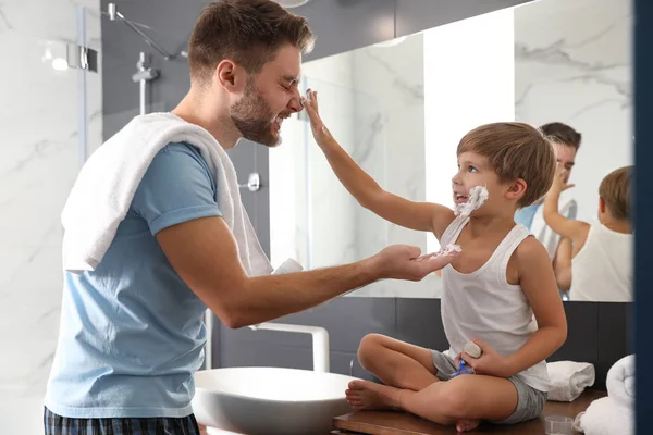 Dad and son with shaving foam on their faces having fun in bathroom