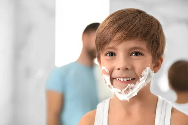 Menino feliz com espuma de barbear no rosto no banheiro, espaço fo — Fotografia de Stock