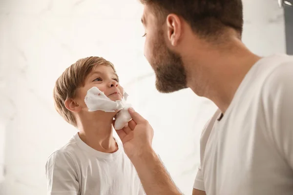 Pai aplicando espuma de barbear no rosto do filho no banheiro — Fotografia de Stock