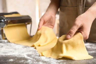 Gri masada hamuru makarna makinesiyle hazırlayan kadın.