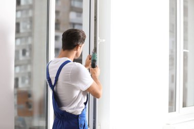 İnşaat işçisi içeride tornavidayla plastik pencereyi tamir ediyor.