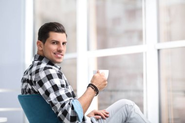 Bir bardak içkili adam evinin penceresinin yanında dinleniyor.