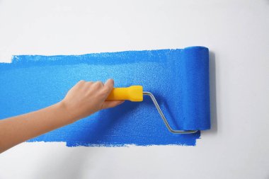 Mavi boyalı beyaz duvarı boyayan kadın, yakın plan. İç yenileme