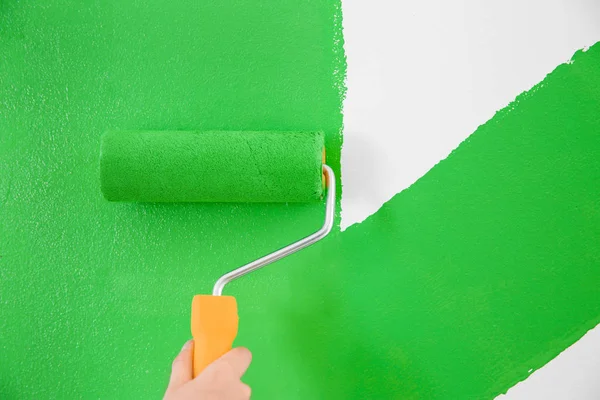 Woman painting white wall with green dye, closeup. Interior renovation