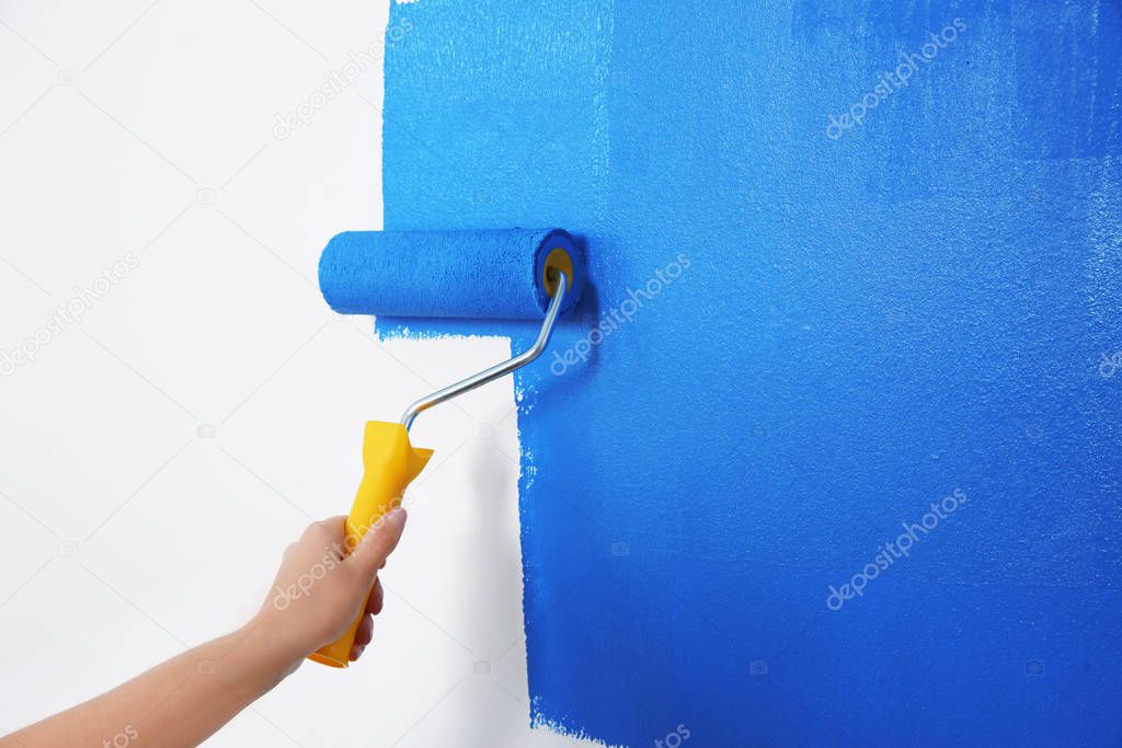 Woman painting white wall with blue dye, closeup. Interior renovation