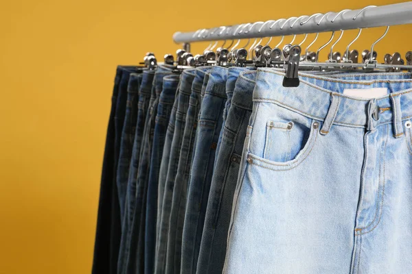 Rack with different jeans on yellow background, closeup — Stock Photo, Image
