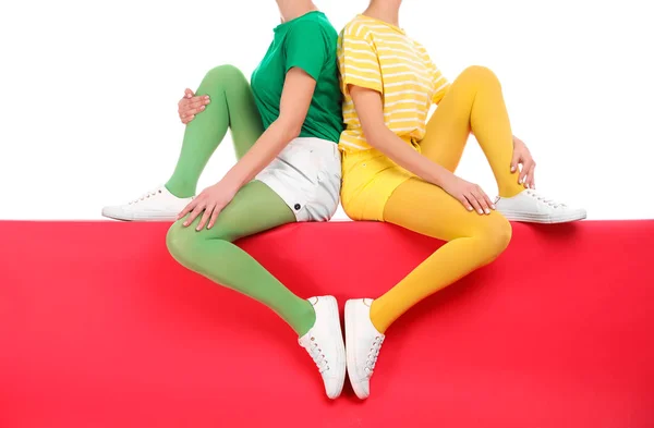 Mujeres con medias brillantes sentadas juntas sobre fondo de color — Foto de Stock