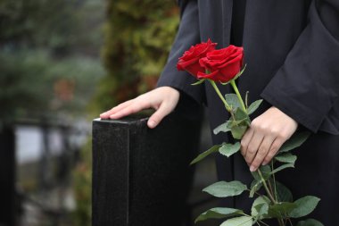 Woman with red roses near black granite tombstone outdoors, clos clipart