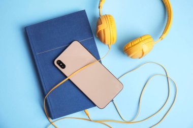 Kitap, modern kulaklıklar ve açık mavi arka planda akıllı telefon.,