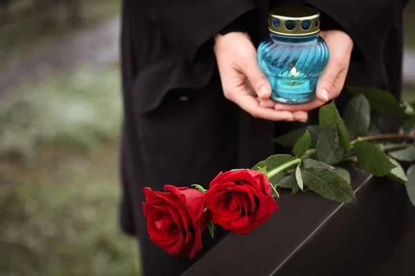 Woman with candle outdoors, focus on red roses. Funeral ceremony