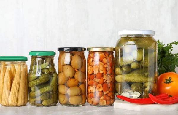 Frascos de vidro com diferentes vegetais em conserva na aba de mármore leve — Fotografia de Stock