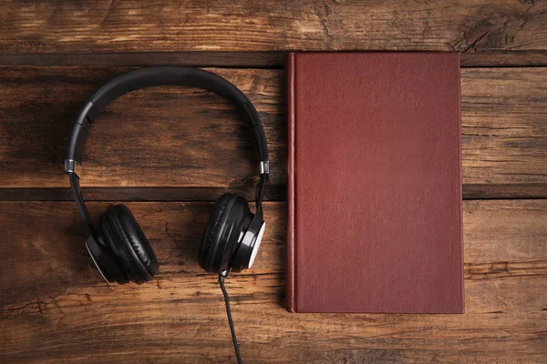 Boek en moderne koptelefoon op houten tafel, plat lay — Stockfoto