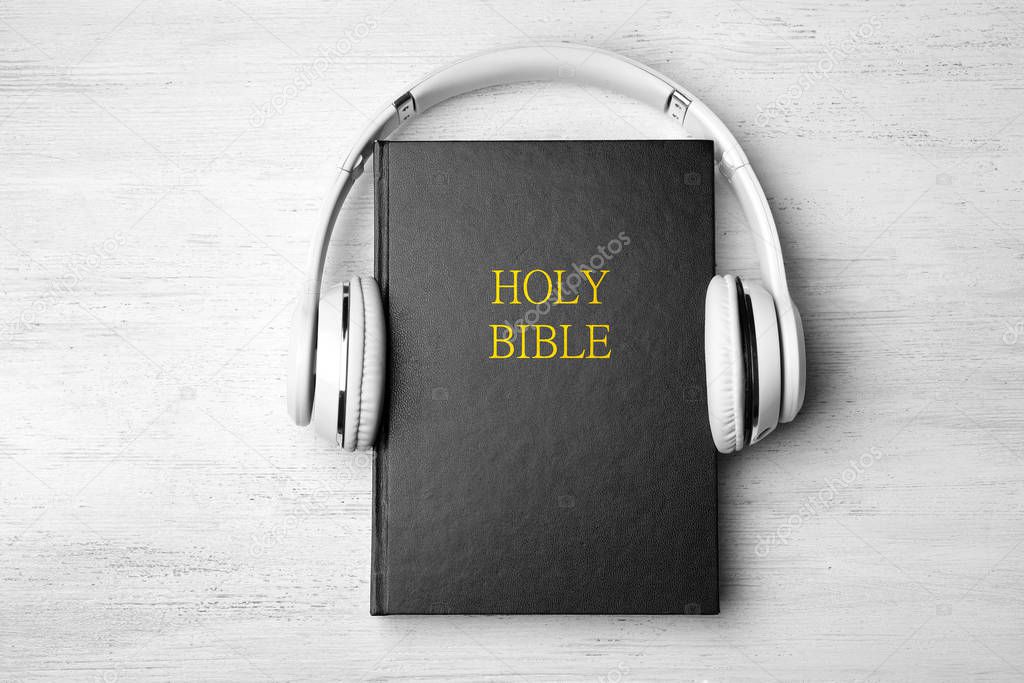 Bible and headphones on white wooden background, top view. Religious audiobook
