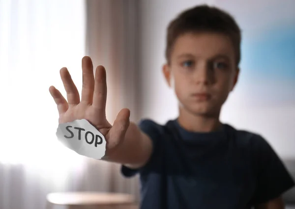 Abused little boy with sign STOP indoors, focus on hand. Domesti — 스톡 사진