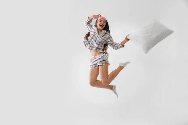 Beautiful woman with pillow jumping on light grey background. Be — 스톡 사진