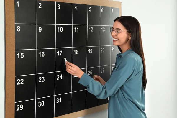 Jeune femme écrivant avec de la craie à bord calendrier — Photo