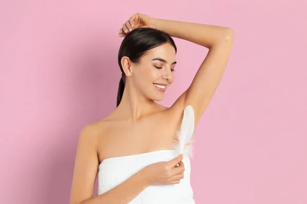 Young woman touching armpit with feather after epilation procedu